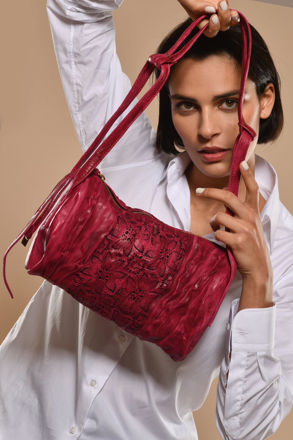 Woman holding a garnet nappa leather handbag against a peach beige background.