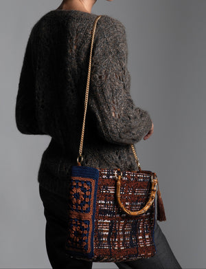 Person wearing a textured knitted sweater with a patterned handbag featuring bamboo handles, crochet flower side panels and chain shoulder strap.