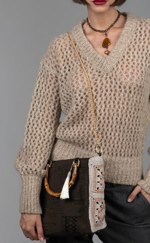 Person wearing a textured taupe knitted sweater with a cotton monument-motif handbag featuring bamboo handles and a diamond-cut metal chain.