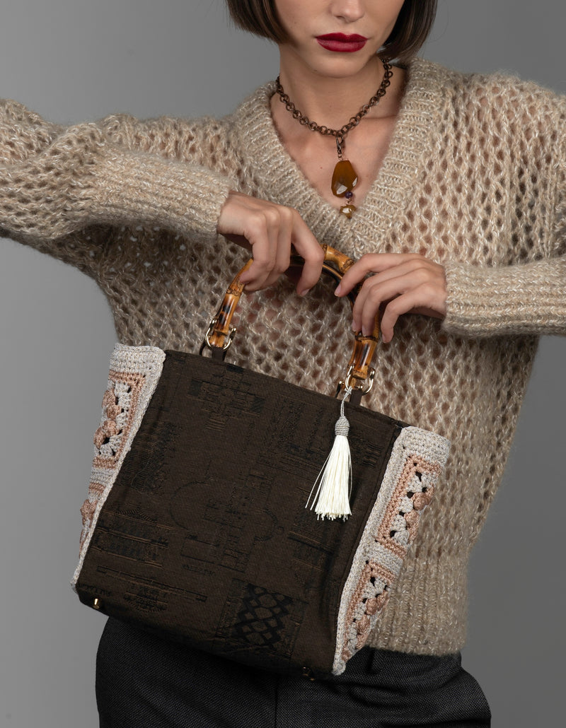Person wearing a textured taupe sweater holding a cotton monument-motif  handbag with crochet flowers.