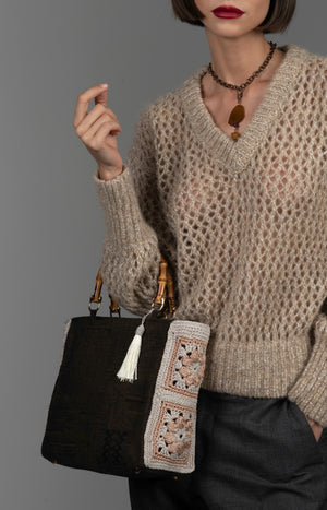 Person wearing a textured taupe sweater holding a cotton monument-motif handbag with bamboo handles and a white silk thread tassel.